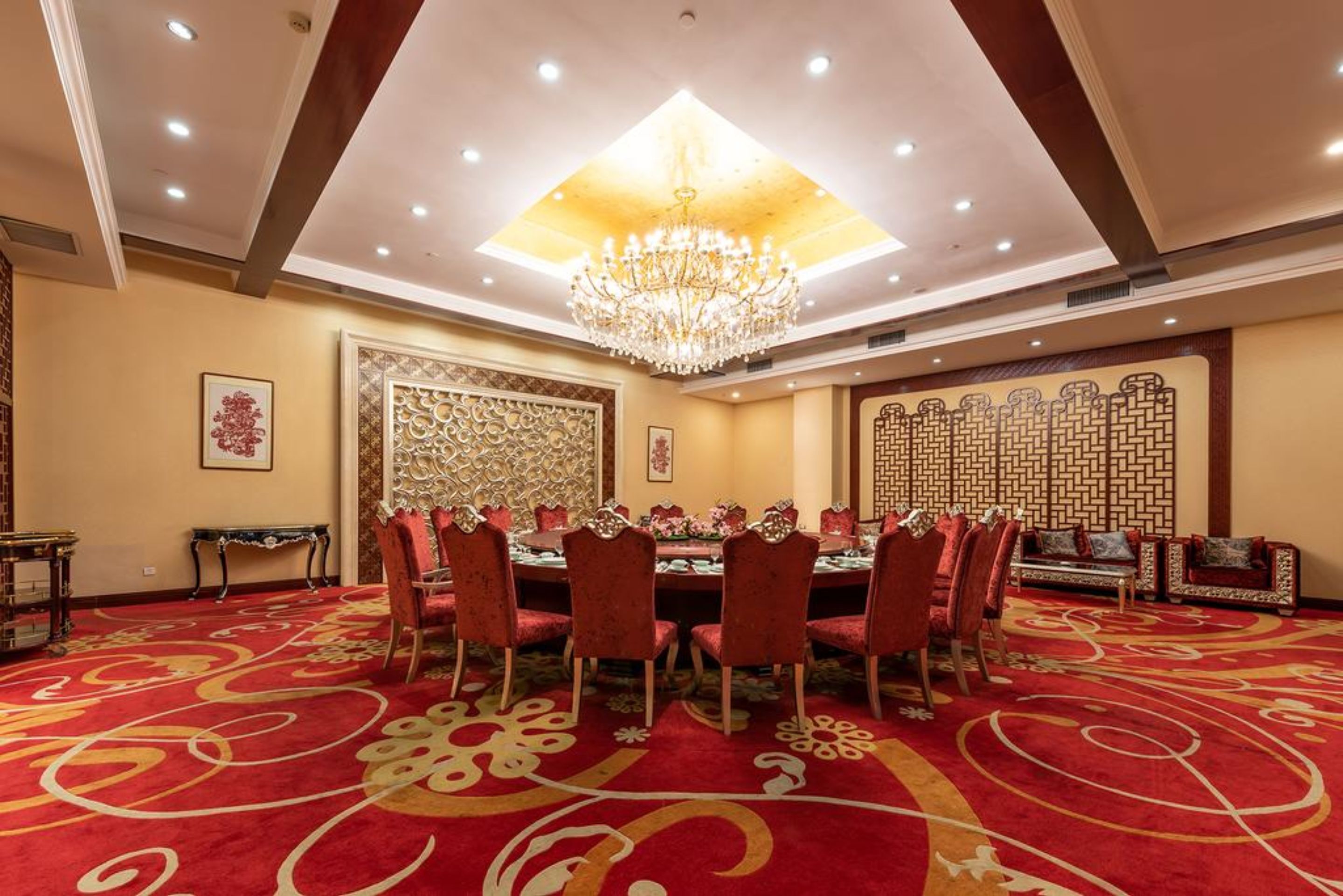 A conference room with a round table, red chairs, a chandelier, and a patterned carpet.