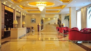 Een hotel lobby met een receptiebalie, rode banken, een kroonluchter en een trap naar de verdiepingen erboven.