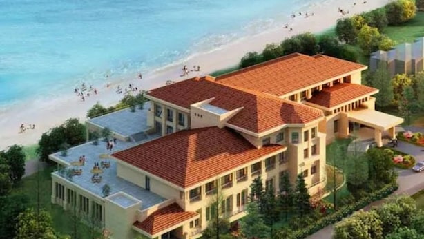 Een groot, meerhoog gebouw met een rode pannendak, gelegen nabij een strand waar mensen in het water zijn.
