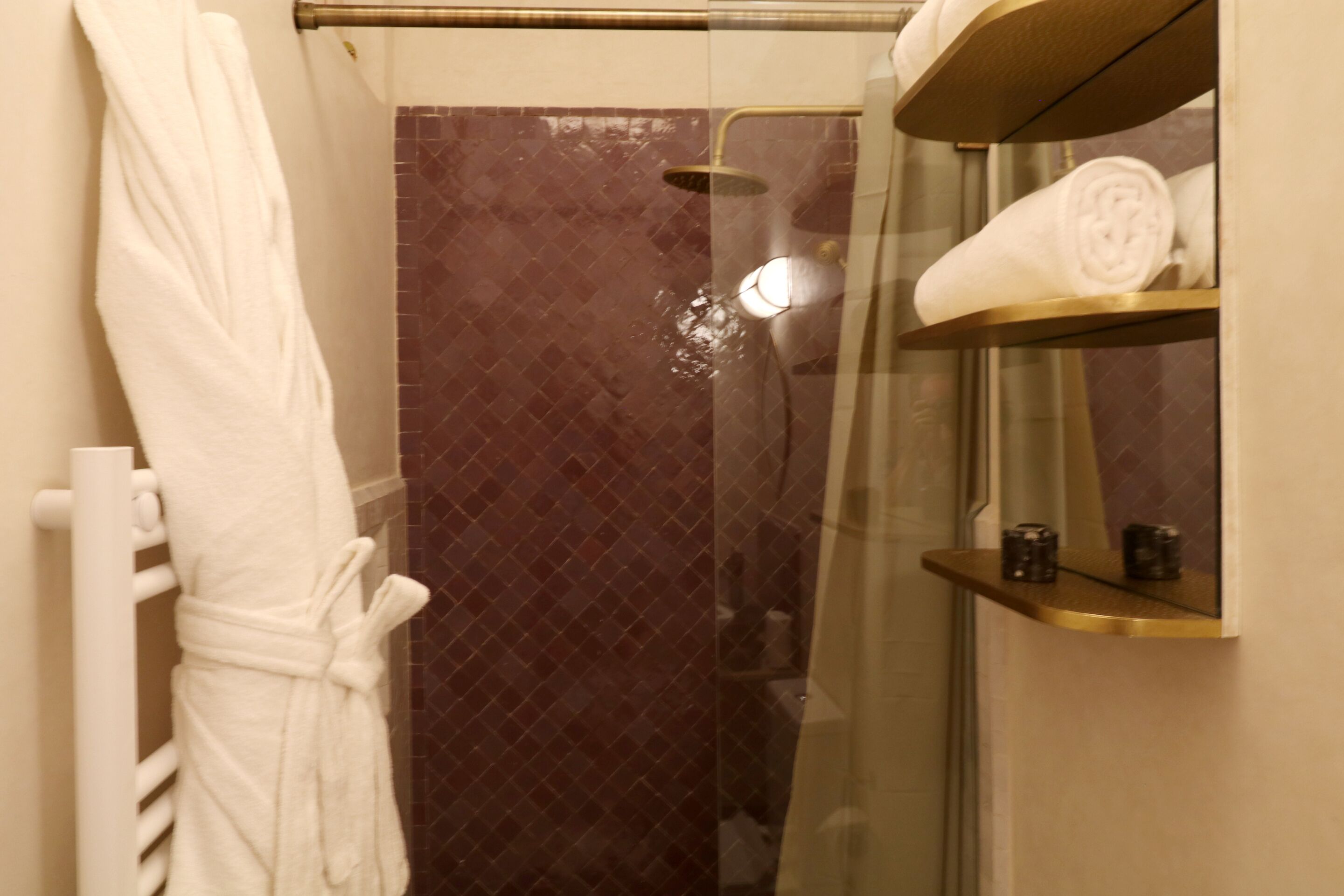 Un baño con cabina de ducha de vidrio, un toallero blanco y un estante con toallas dobladas.
