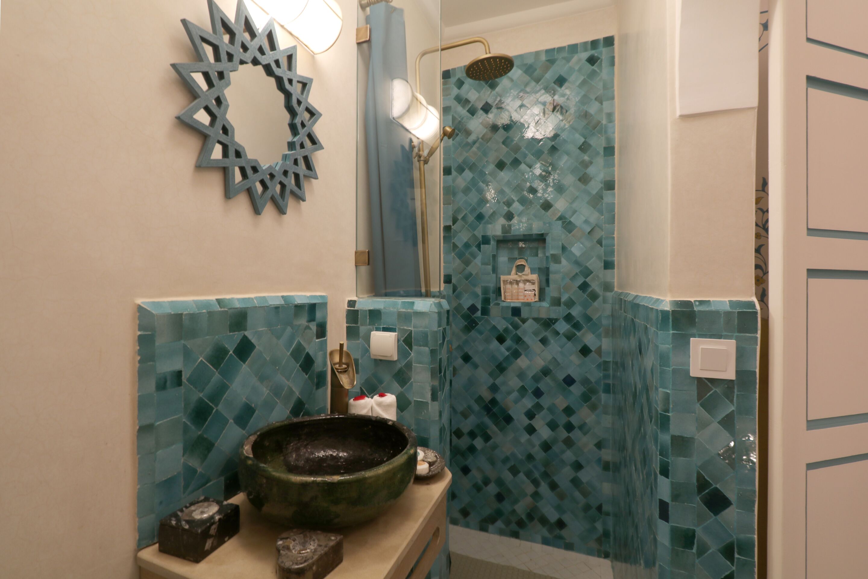 Une salle de bain avec un mur recouvert de mosaïques, un grand vase décoratif posé sur le comptoir et un espace douche.
