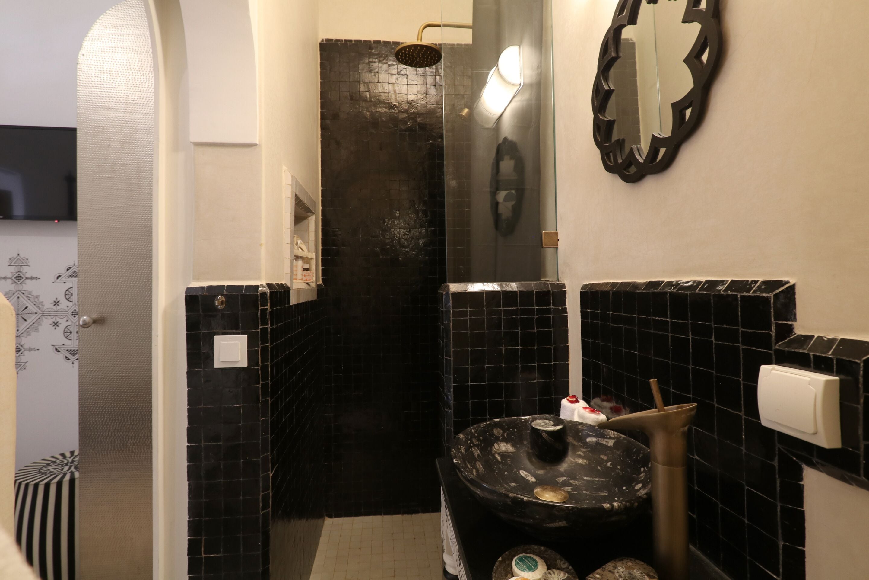 Un baño con paredes de azulejos negros, zona de ducha y lavamanos con dispensador de toallas.