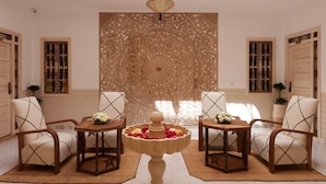A room with two armchairs, a wooden table with a flower centerpiece, and a decorative wall panel. - Riad Mareme & Spa (Marrakech)