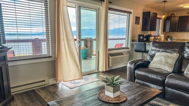 A modern living room with a leather sofa, a coffee table with a plant, and large windows with blinds. - Edgewater #5 Montana (Polson)