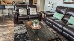 A living room with a dark brown leather sofa, a coffee table with a plant, and a kitchen in the background. - Edgewater #5 Montana (Polson)