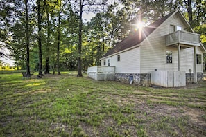 A single-story house with a balcony, surrounded by a grassy yard and trees. - Peaceful Broken Bow Cottage w/ Fire Pit! (Broken Bow)