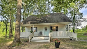 Une maison à deux étages avec un porche à l’avant, des fondations en pierre et un grand arbre devant.
