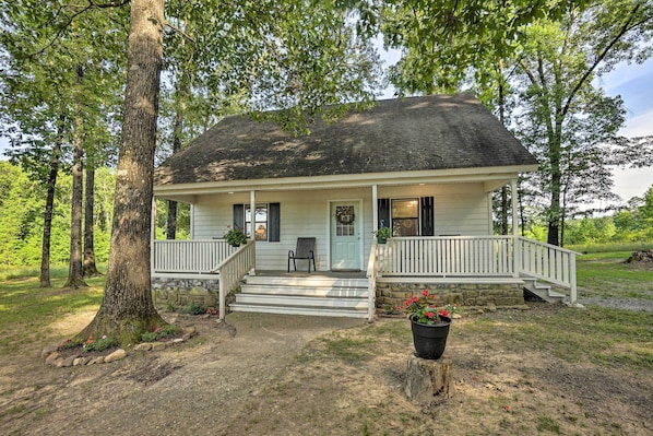 A two-story house with a front porch, a stone foundation, and a large tree in front. - Peaceful Broken Bow Cottage w/ Fire Pit! (Broken Bow)