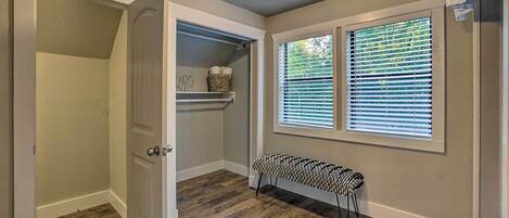 A hallway with a bench, a door leading to a closet, and a window with blinds.