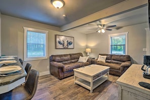 A living room with two brown leather sofas, a white coffee table, and a dining area with a table set for four. - Peaceful Broken Bow Cottage w/ Fire Pit! (Broken Bow)
