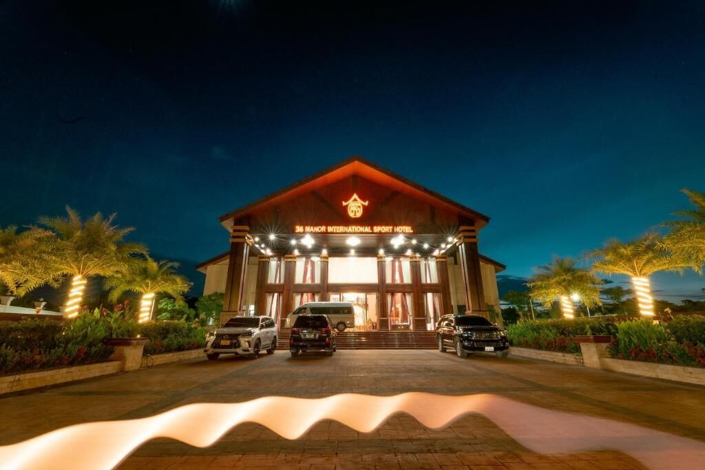 A hotel entrance with a sign reading '36 Manor International Sport Hotel,' a covered driveway, and parked cars.