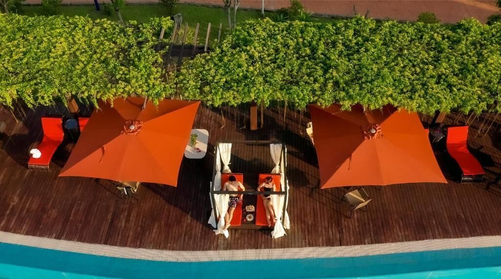 A poolside area with sun loungers and umbrellas, surrounded by greenery.