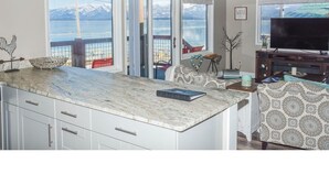 A kitchen with a large island, two pendant lights, a view of a lake with mountains, and a dining area with patterned upholstery. - Edgewater #8 Scout (Polson)