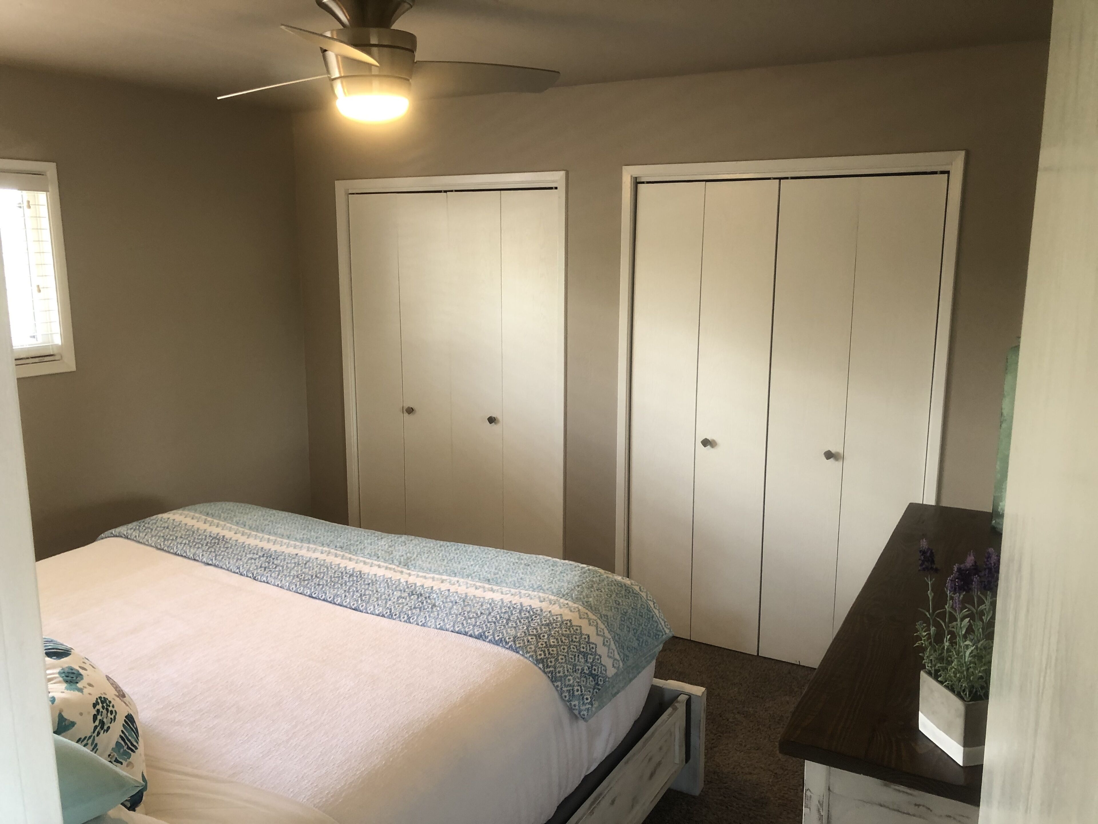 A bedroom with a bed, two wardrobes, a ceiling fan, and a small table with a plant.