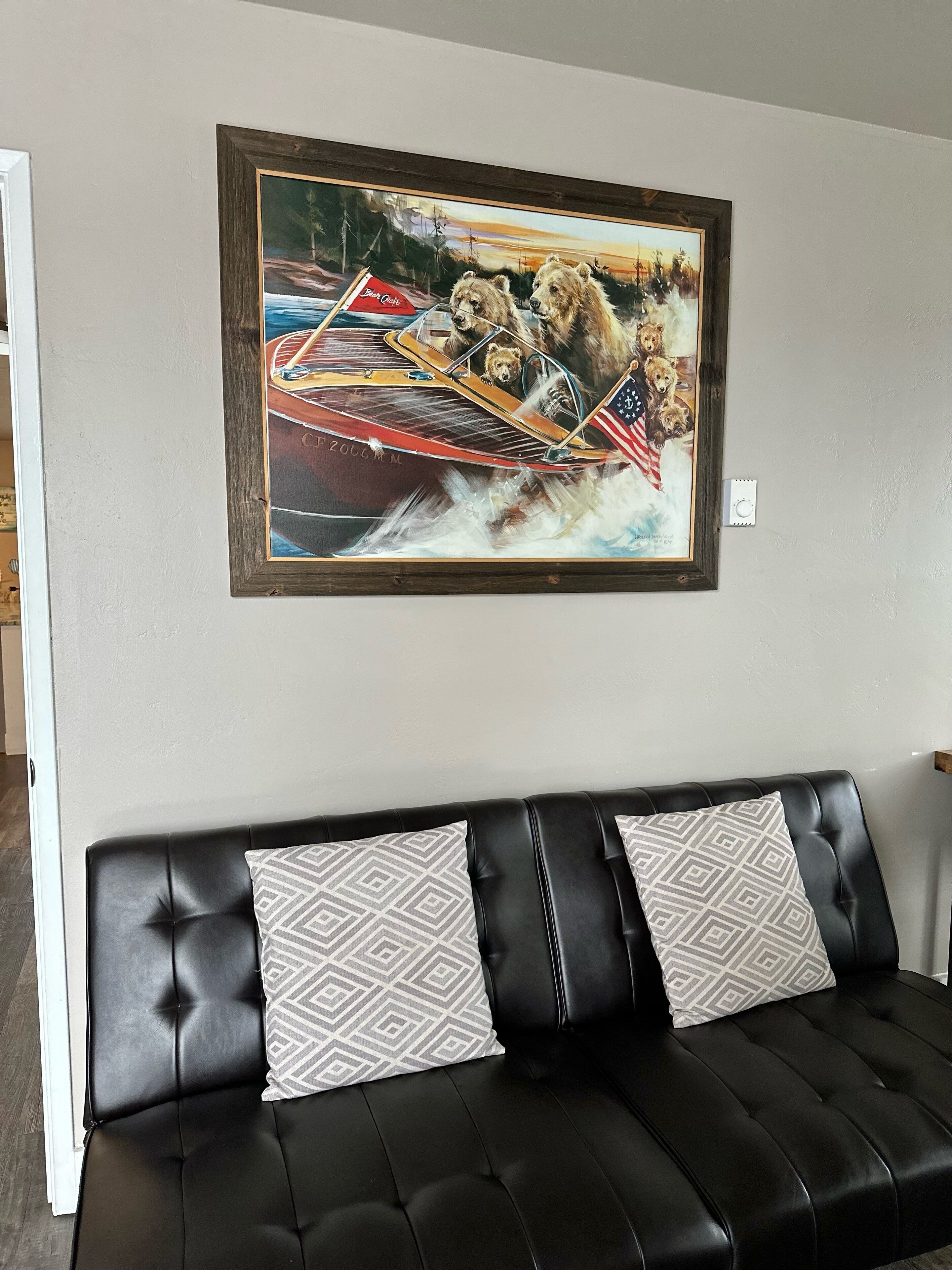 Ein Wohnzimmer mit einer schwarzen Ledersofa, zwei gemusterten Zierkissen und einem gerahmten Gemälde von einem Boot mit Bären und einer amerikanischen Flagge.