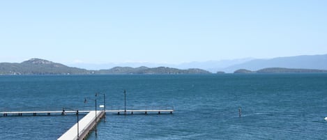 Un molo si protende in un lago tranquillo, con montagne lontane sotto un cielo sereno.