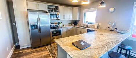 A modern kitchen with stainless steel appliances, a large island, pendant lighting, and a view of the outdoors.