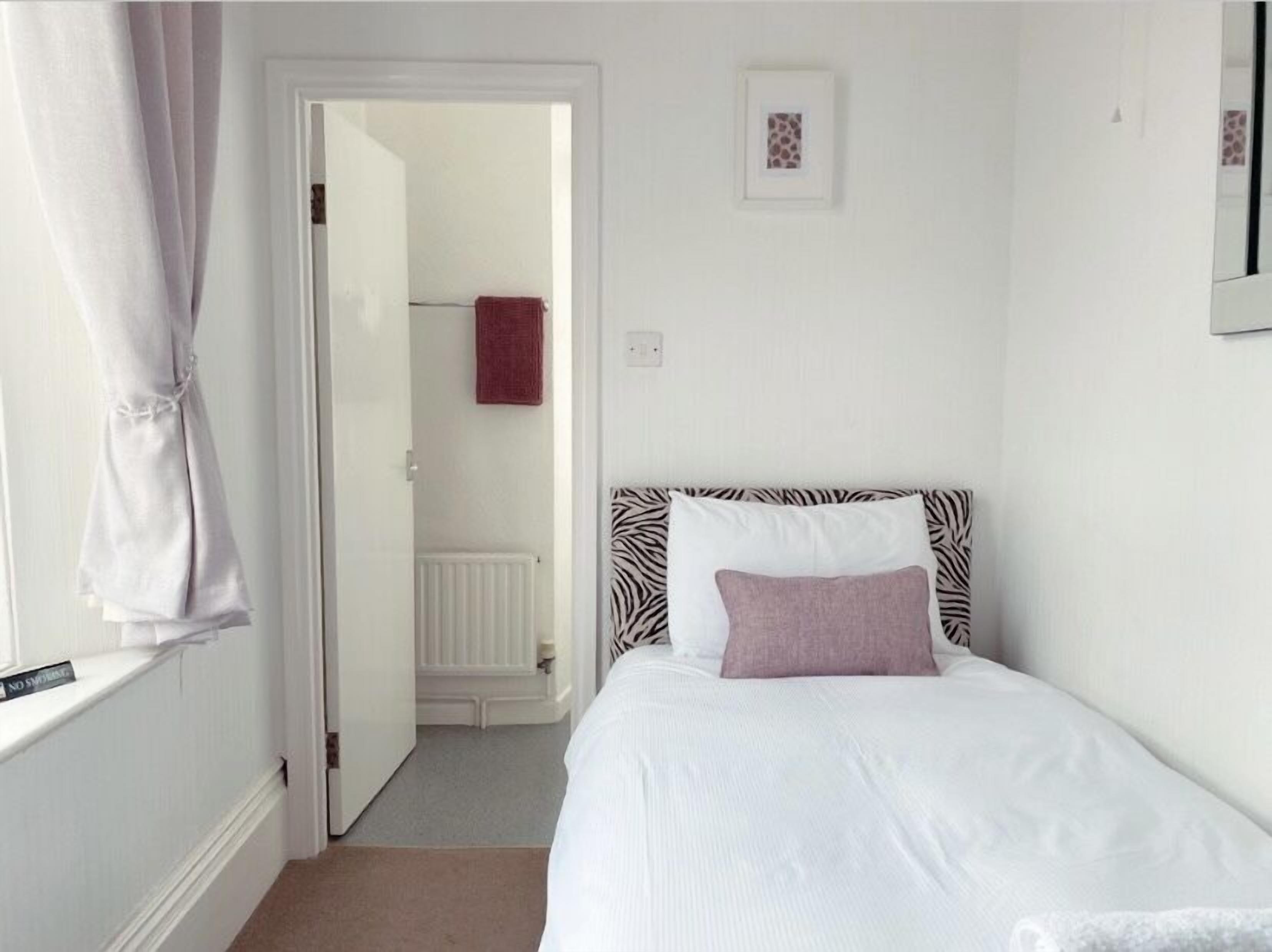 A bedroom with a bed, a door leading to a bathroom, and a small framed picture on the wall.
