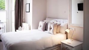 A neatly arranged bedroom with a large bed, bedside tables, a nightstand, a mirror, and a window with curtains. - The Rosewood Torquay (Torquay)