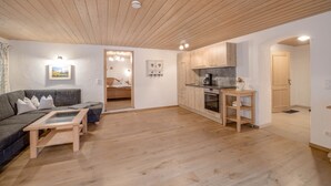 A modern living room with a sofa, coffee table, and kitchen area with wooden cabinets and a stove. - Apartment Waxenstein with Balcony, Mountain View & Wi-Fi (Grainau)