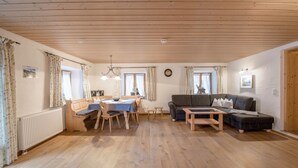 A spacious living area with a wooden floor, a dining table, a sofa, and a chandelier. - Apartment Waxenstein with Balcony, Mountain View & Wi-Fi (Grainau)