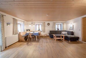 Un vaste espace de vie doté d’un plancher en bois, d’une table à manger, d’un canapé et d’un lustre.