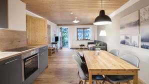 A modern kitchen with wooden cabinets, a dining table with chairs, and a large pendant light. - Apartment Zugspitze with Terrace, Mountain view & Wi-Fi (Grainau)