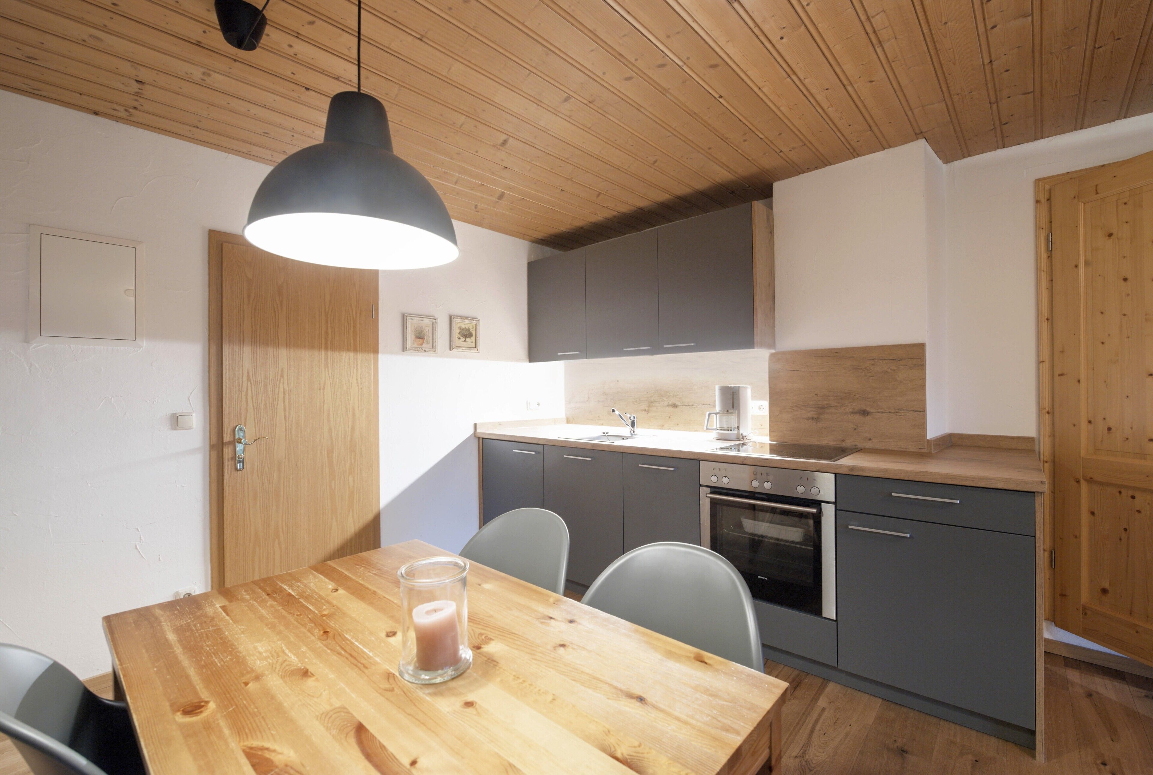 Une cuisine moderne avec un plafond en bois, des meubles de couleur grise, une table à manger en bois et un luminaire suspendu.