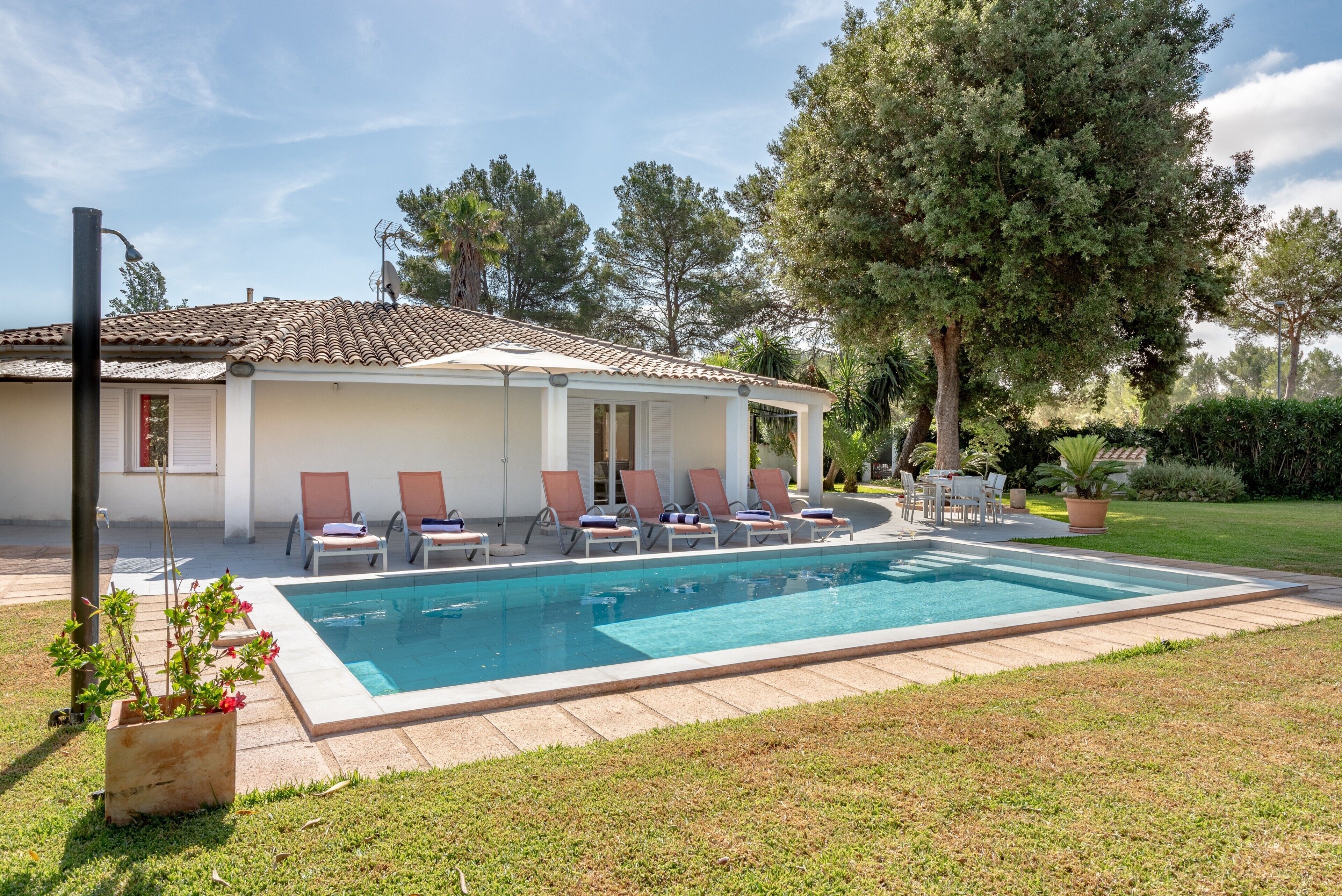 A poolside area with lounge chairs, a pool, and a building with a tiled roof.