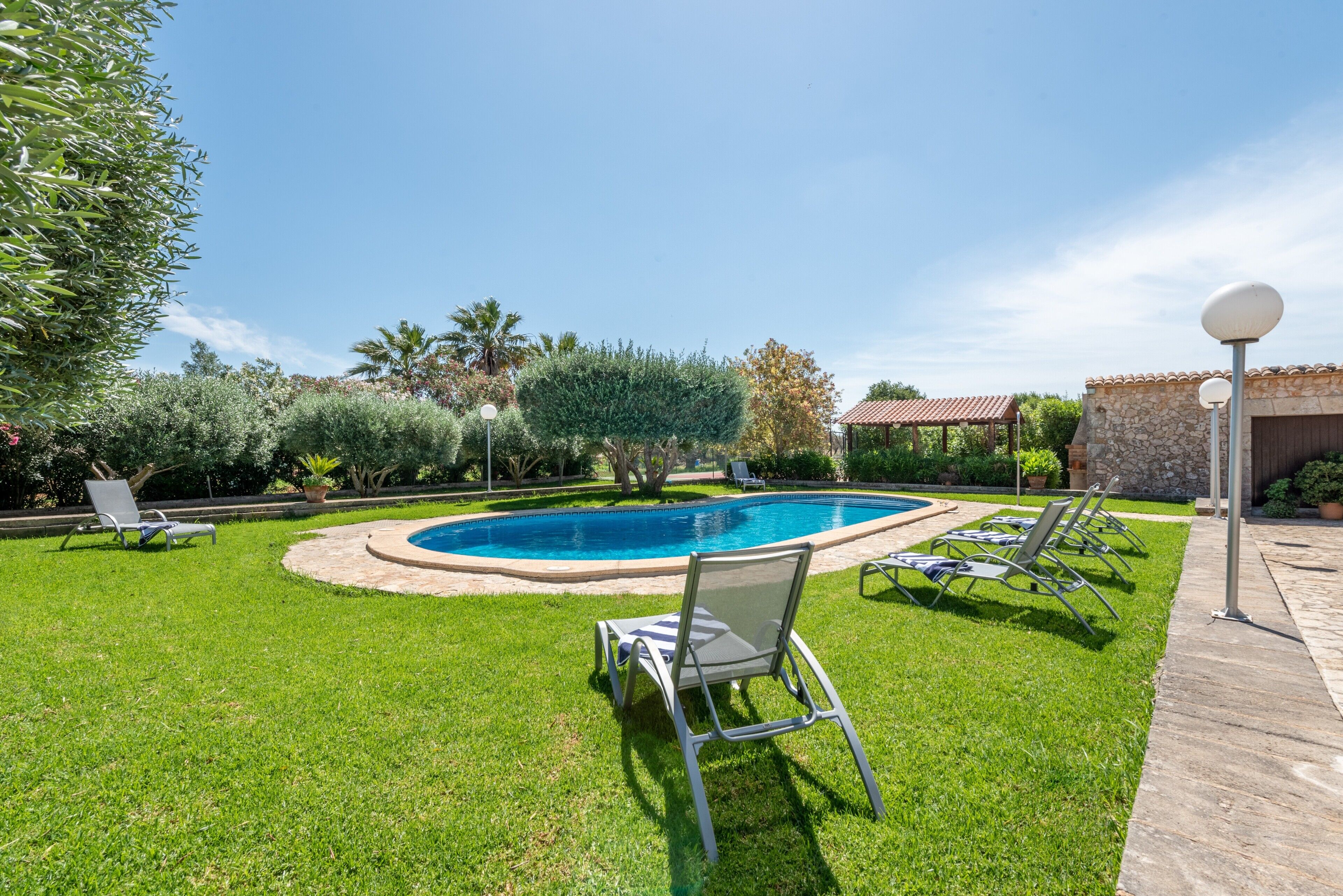 A swimming pool with a grassy area, lounge chairs, and a stone building with a tiled roof.