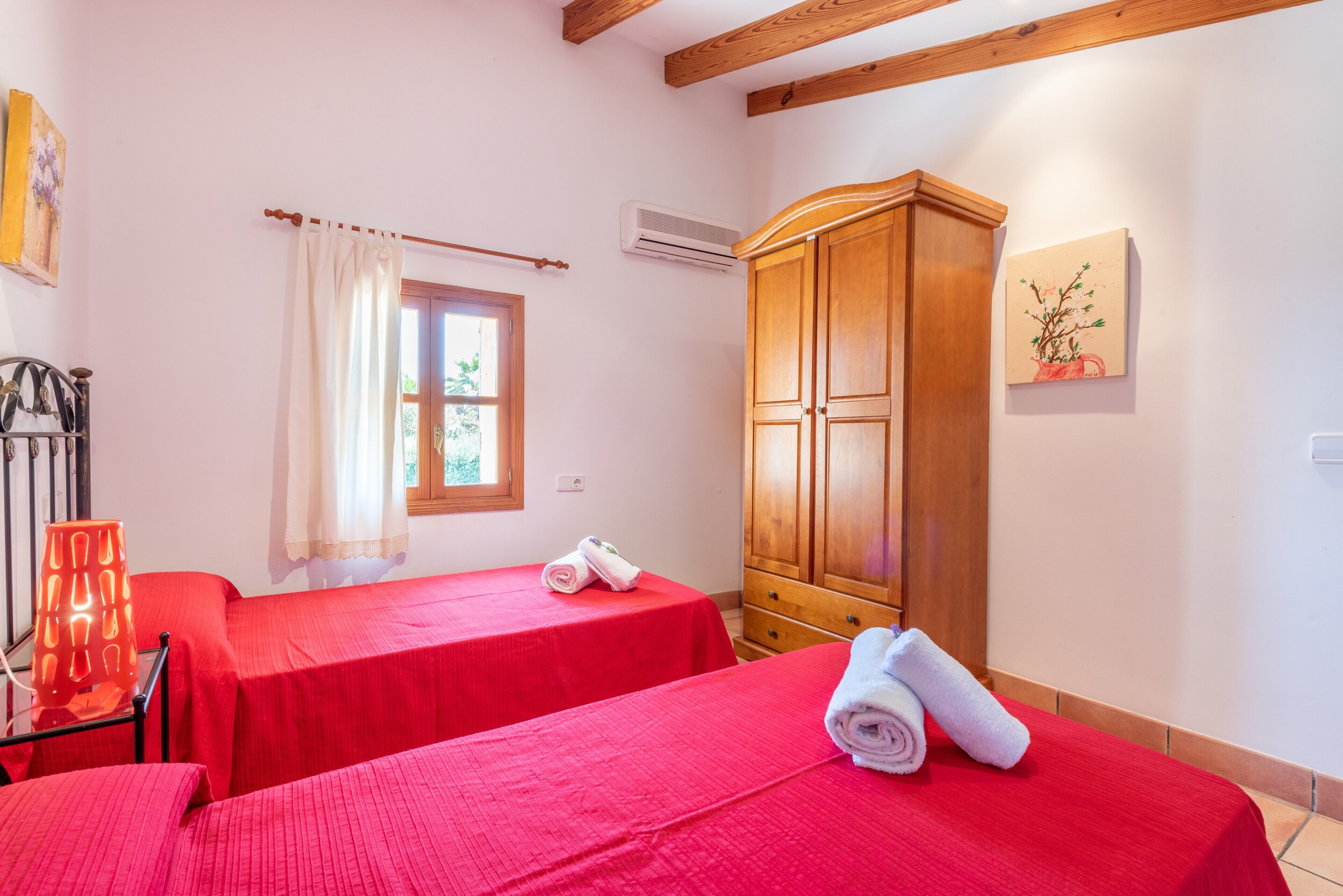 A hotel room with two beds, a wooden wardrobe, a window with curtains, and a wall-mounted air conditioner.