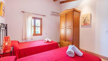 A hotel room with two beds, a wooden wardrobe, a window with curtains, and a wall-mounted air conditioner.
