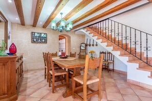 A dining area with a wooden table and chairs, a chandelier, and a staircase with a wrought iron railing.