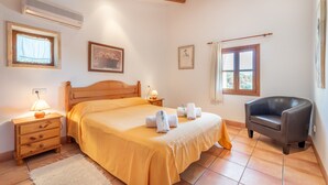 Une chambre à coucher avec un lit, une table de chevet, une lampe, des tableaux encadrés, une chaise et une fenêtre.