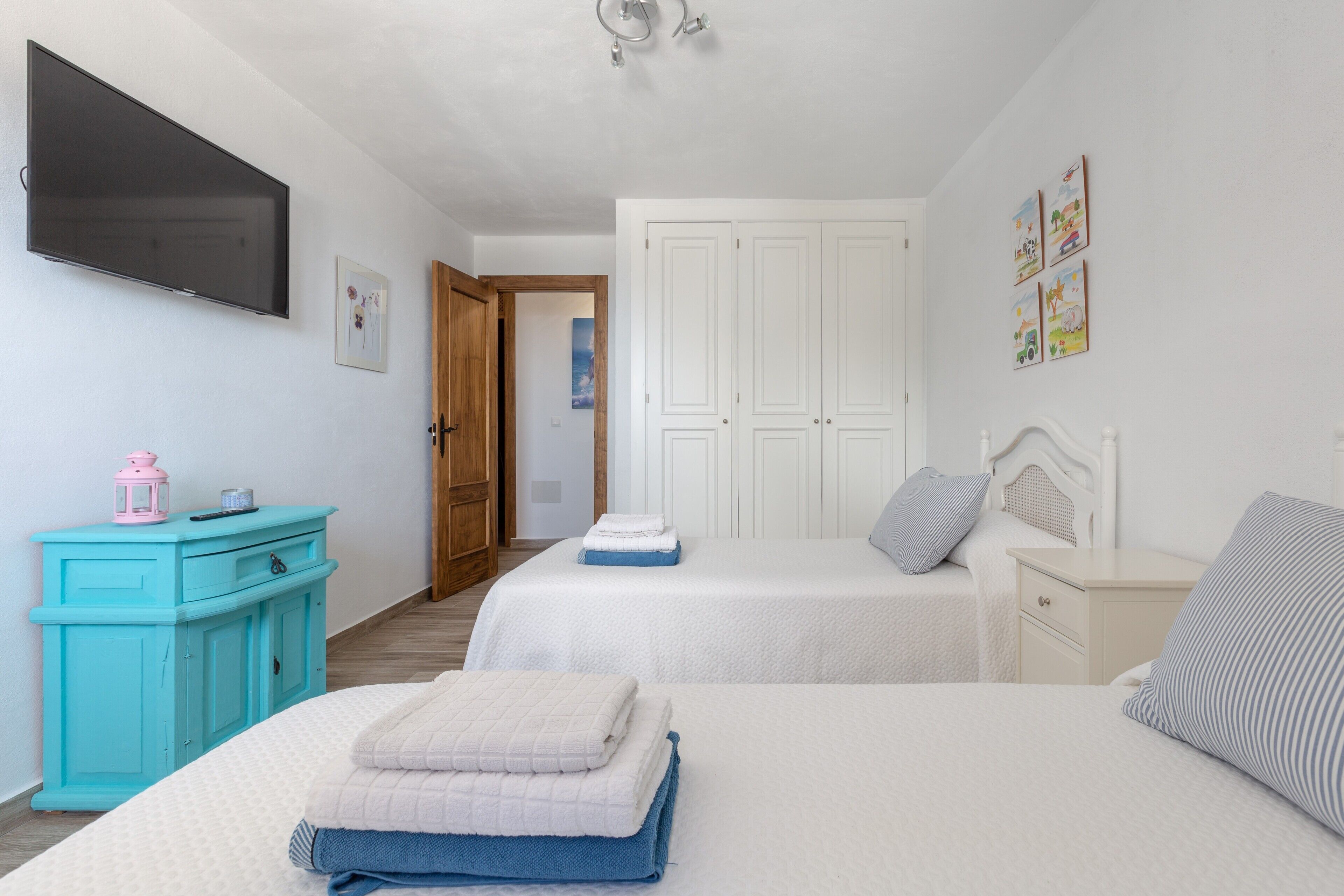 A bedroom with two beds, a TV, a wardrobe, and a door leading to another room.