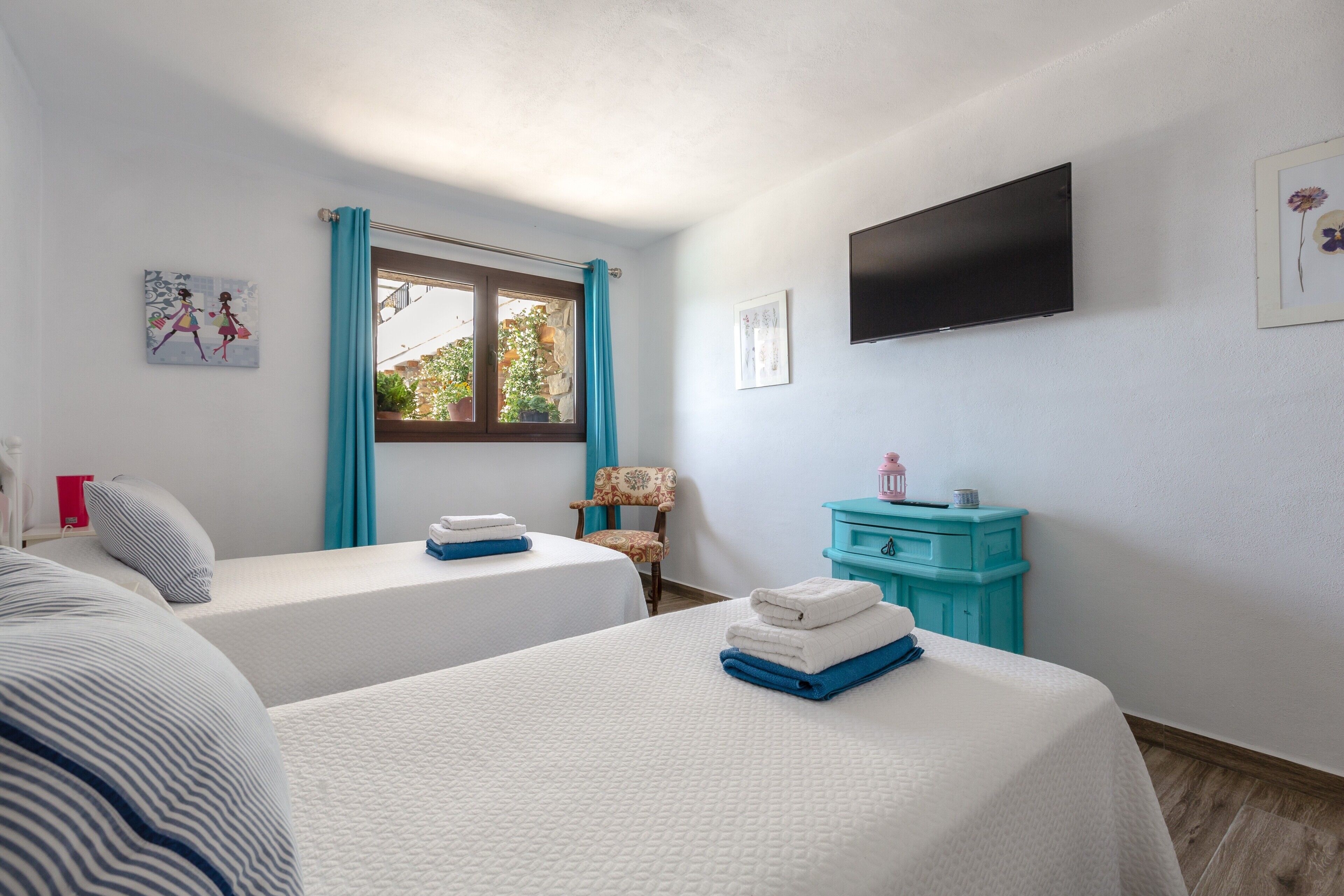 Un dormitorio con dos camas, una ventana con cortinas, un televisor en la pared y un pequeño aparador.