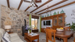 A stone wall, wooden ceiling beams, a dining table with chairs, a sofa, a TV, and a clock. - Luxury Villa Casa el Impero with Pool, Terrace, Unique Mountain View and WiFi (Gaucin)