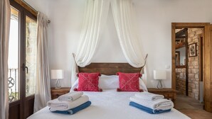 A bedroom with a large bed, two bedside tables, a wooden headboard, and a stone wall. - Luxury Villa Casa el Impero with Pool, Terrace, Unique Mountain View and WiFi (Gaucin)