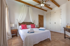 Une chambre à coucher comprenant un lit, des rideaux, un plafond en bois, une table de chevet, une commode et une armoire.