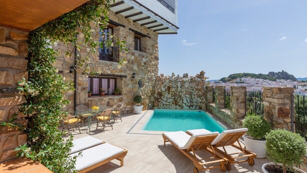 A stone building with a pool, outdoor seating, and a view of a distant town. - Luxury Villa Casa el Impero with Pool, Terrace, Unique Mountain View and WiFi (Gaucin)