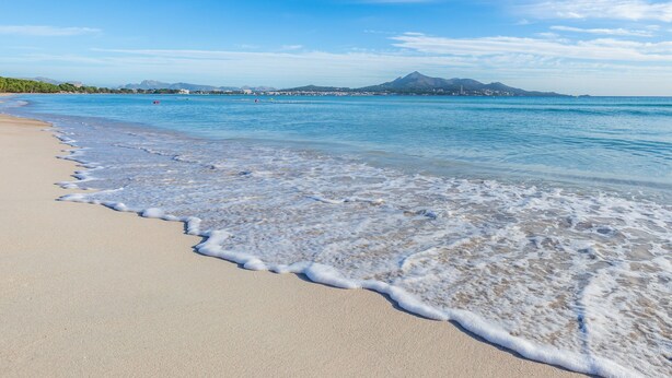 A beach with clear water, a sandy shore, and a mountain in the distance. - “Ca Na Rosa” close to the Beach with Wi-Fi, A/C, Terrace, Garden & Pool (ALCUDIA)