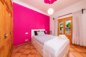 A room with a bed, a wooden wardrobe, a window with curtains, and a view of greenery outside.