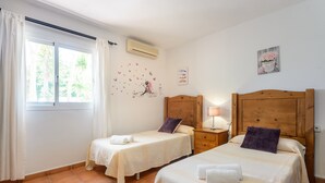 A bedroom with two beds, a window with curtains, an air conditioner, and wall decorations. - Holiday Apartment "Can Jordi" with Mountain Views (Sant Josep de sa Talaia)