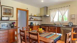 A kitchen with wooden cabinets, a microwave, a coffee maker, and a dining area with chairs and a table. - Holiday Apartment "Can Jordi" with Mountain Views (Sant Josep de sa Talaia)