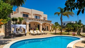 A swimming pool with lounge chairs, a building with arches, and palm trees. - Holiday Apartment "Can Jordi" with Mountain Views (Sant Josep de sa Talaia)
