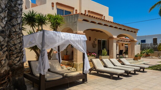 A poolside area with lounge chairs and a covered seating area, surrounded by potted plants and a building with arches. - Holiday Apartment "Can Jordi" with Mountain Views (Sant Josep de sa Talaia)