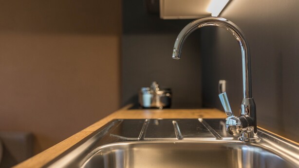 A stainless steel kitchen sink with a modern faucet, a wooden countertop, and a small appliance in the background.