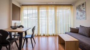 A room with a dining table, chairs, a sofa, and a window with curtains.