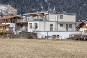 Un bâtiment moderne à deux étages, doté de balcons, d’une terrasse en bois et offrant une vue sur un paysage montagneux.