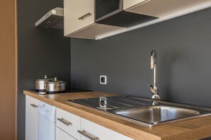 Une cuisine moderne dotée d’un évier en acier inoxydable, d’un plan de travail en bois et de meubles blancs.